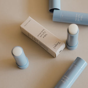 Several blue Tallow Lip Love hydrating lip balm tubes and one white product box labeled Toups and Co Organics are arranged on a beige surface.