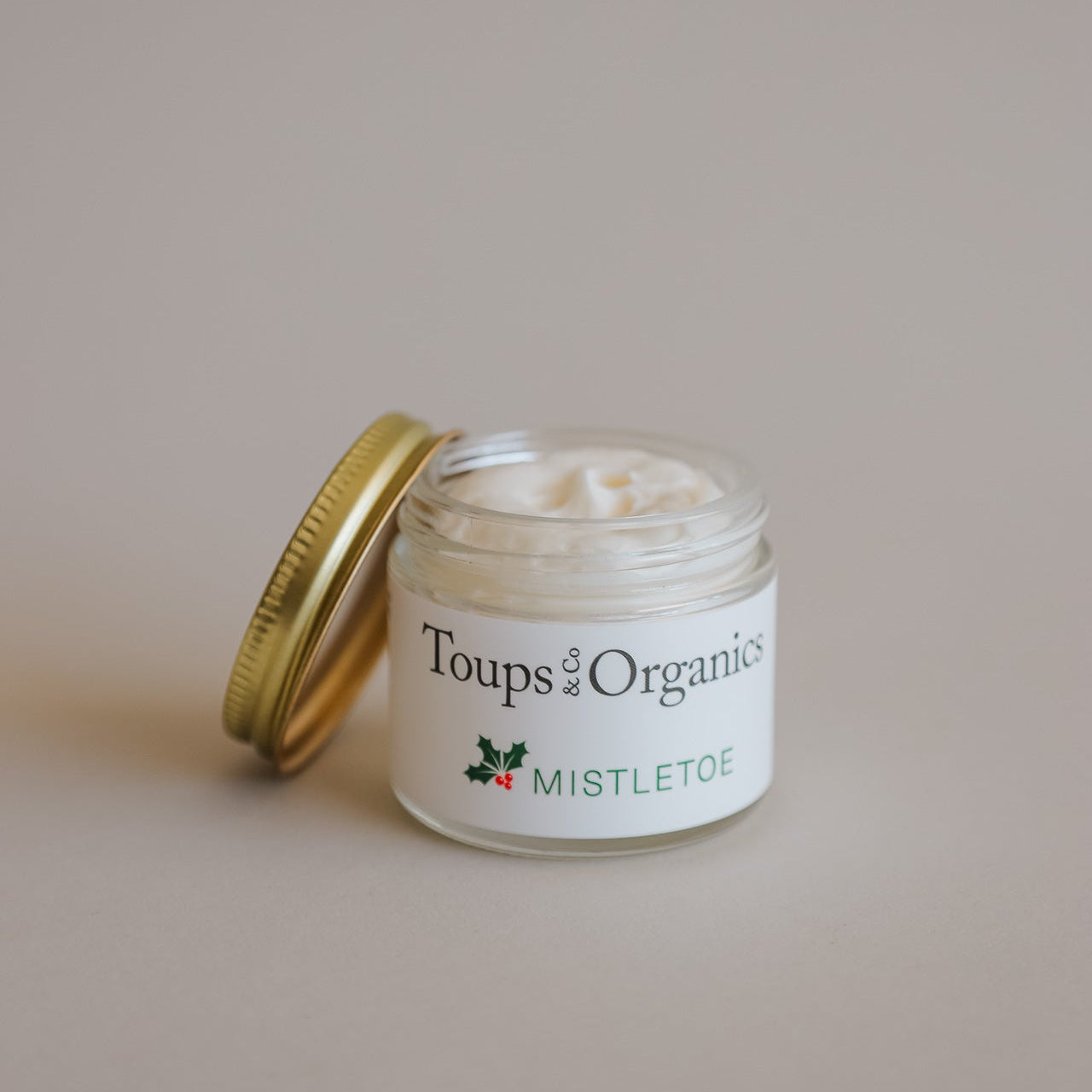 A small glass jar of Toups and Co Organics Mistletoe Balm with a gold lid contains a creamy white tallow balm, ideal as a thoughtful Christmas gift.
