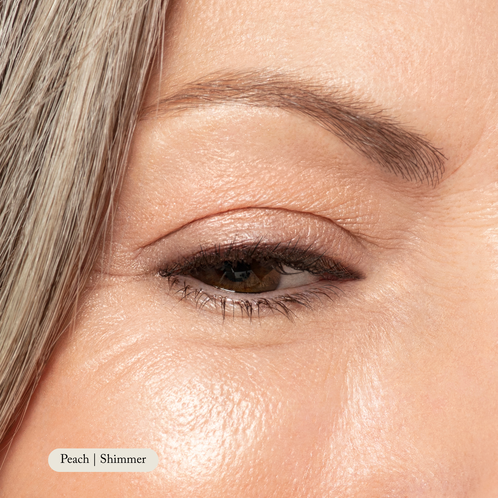 Close-up of an eye wearing Toups and Co Organics Natural Eyeshadow Singles in a peach shimmer shade—highly pigmented color with groomed eyebrow, detailed skin texture, and a touch of gray hair. Text reads: Peach | Shimmer.
