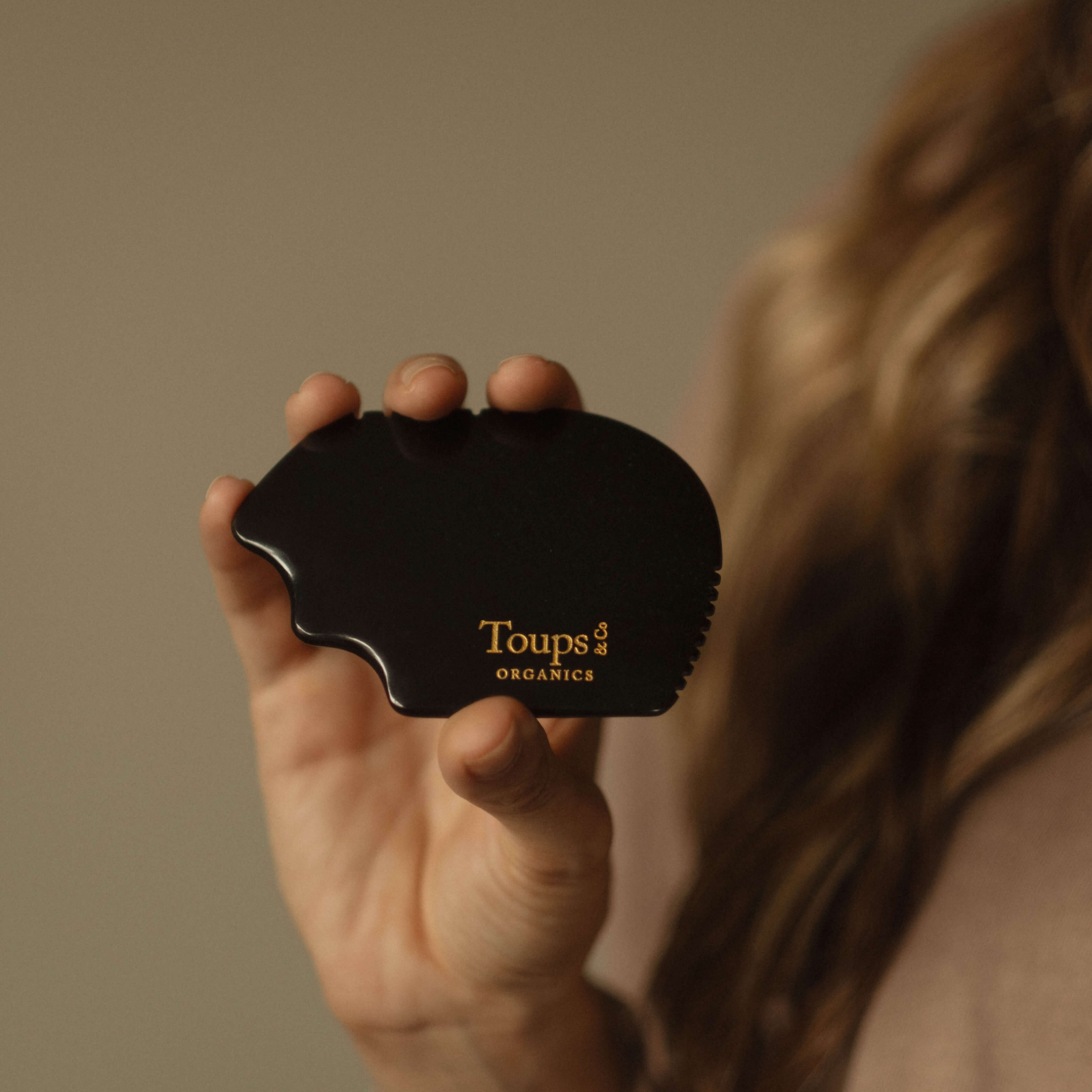 A hand holds the Nephrite Gua Sha by Toups and Co Organics, featuring gold lettering, ideal for lymphatic drainage massage against a subtle background.