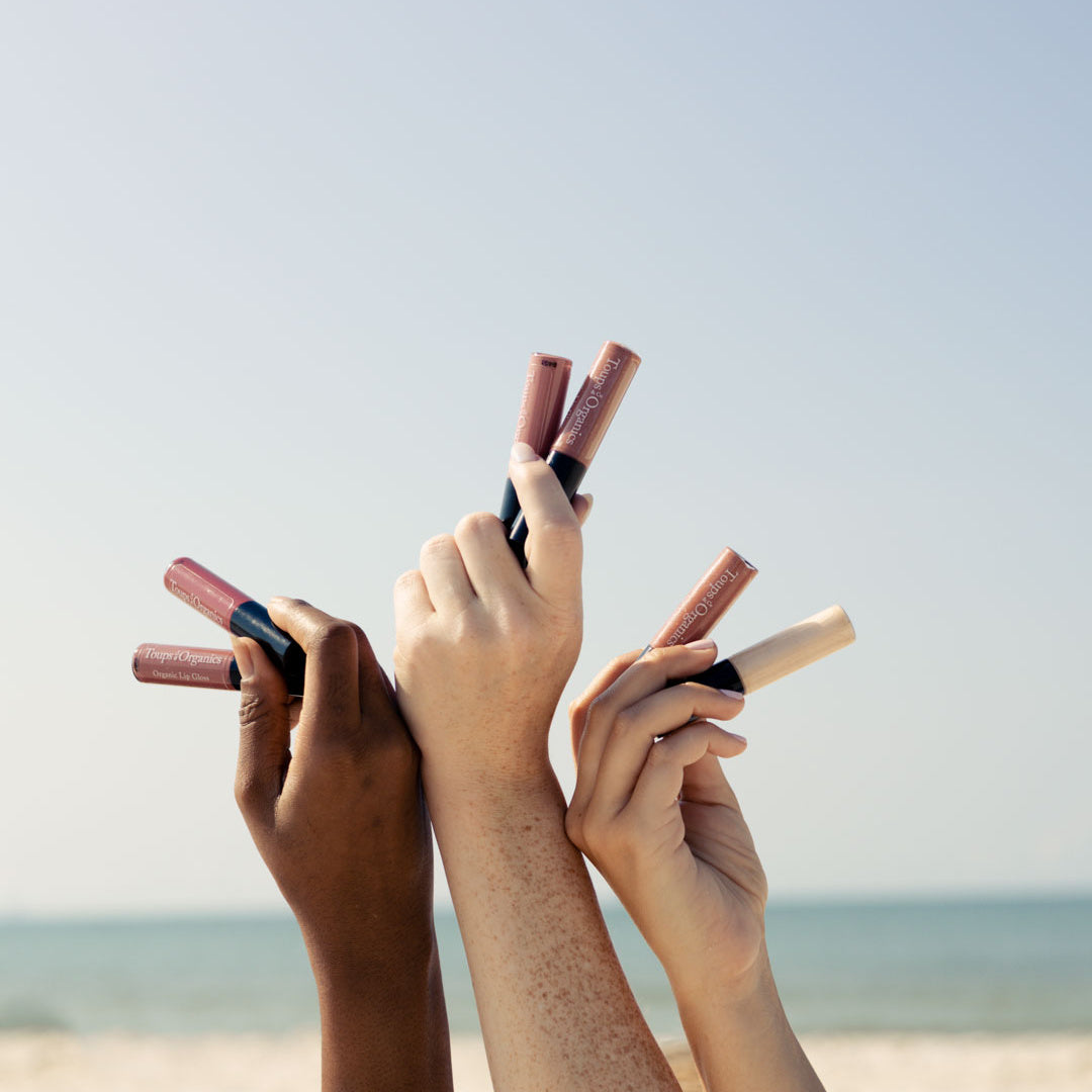 women-hold-up-organic-lip-gloss-against-ocean-background