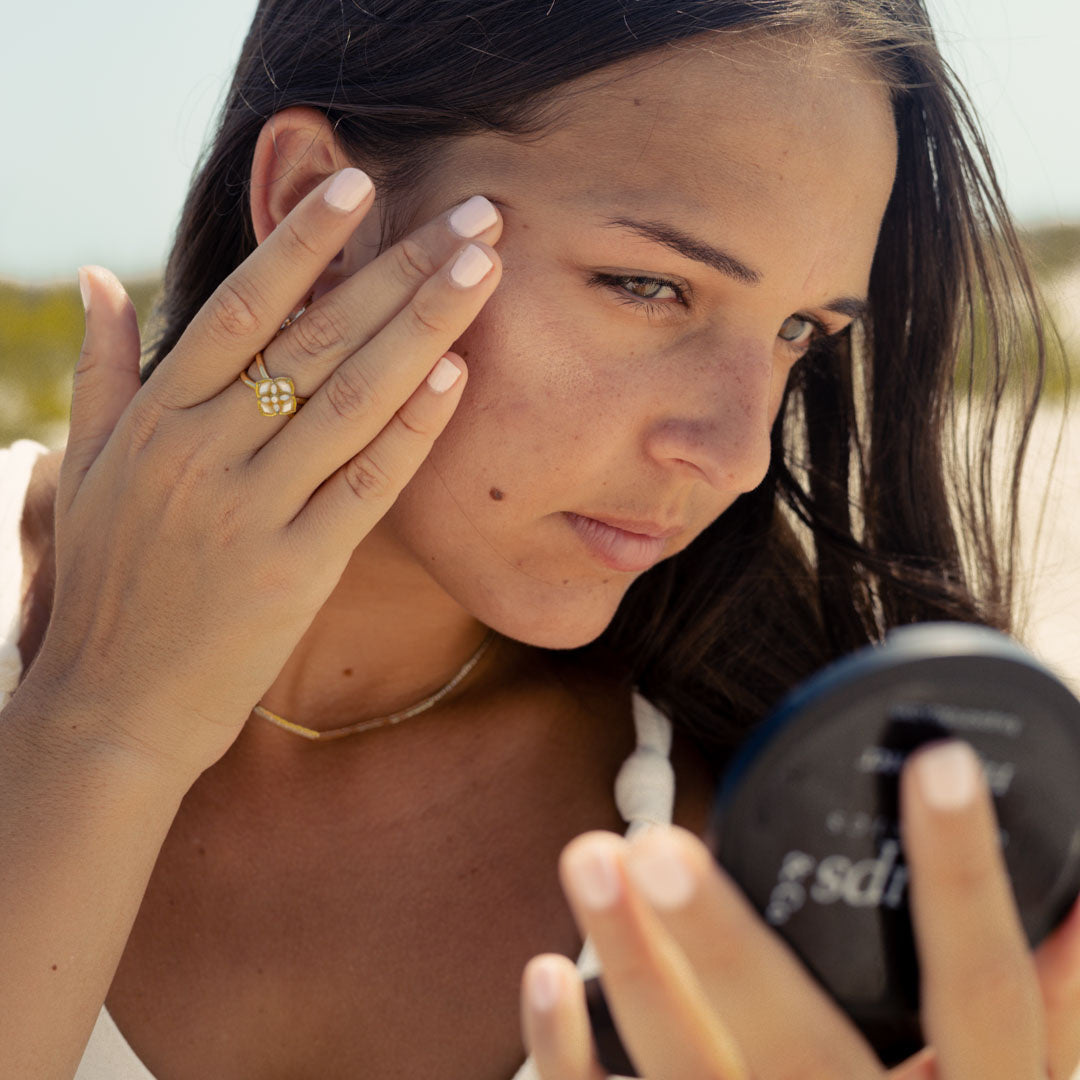 woman-looks-in-mirror-while-applying-nontoxic-makeup-highlighter