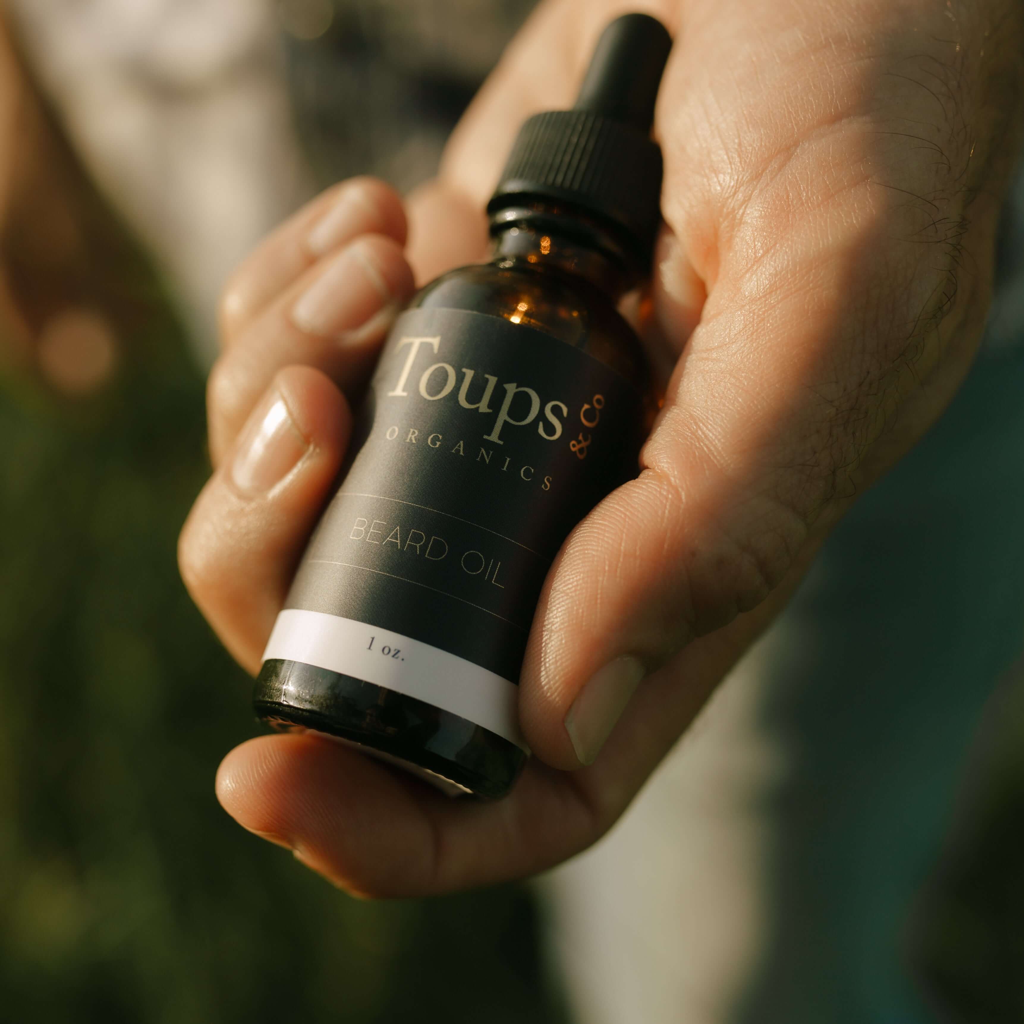hand-holds-nontoxic-beard-oil-for-men-against-a-nature-background