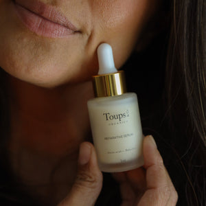 A person holds a bottle of Toups and Co Organics Clean Serum Set with a dropper near their face.
