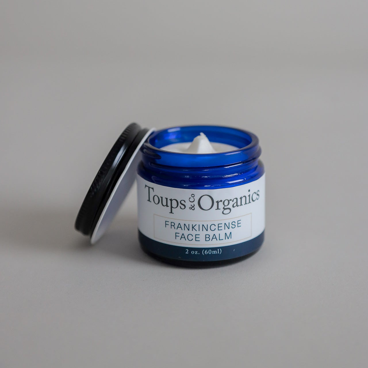 An open jar of tallow balm infused with frankincense essential oil, with the lid resting beside the jar.