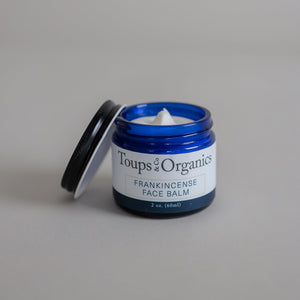 An open jar of tallow balm infused with frankincense essential oil, with the lid resting beside the jar.