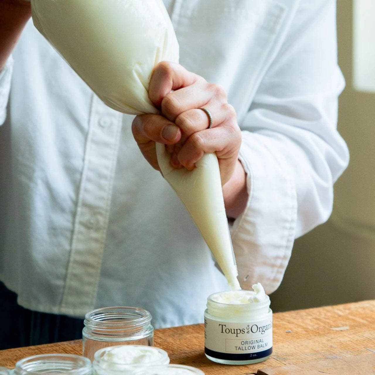 Person piping Toups and Co. Original Tallow Balm into a small glass jar.