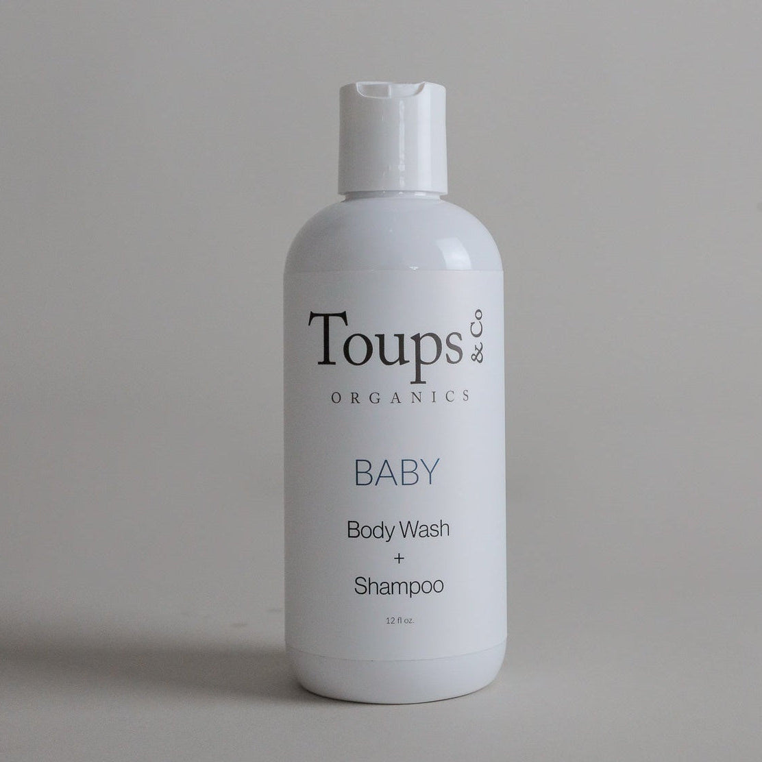 A white bottle labeled Toups and Co Organics Baby Wash + Shampoo, featuring non-toxic ingredients, stands upright against a plain gray background.