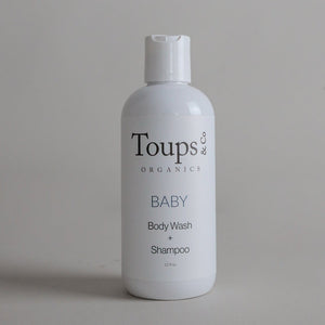 A white bottle labeled Toups and Co Organics Baby Wash + Shampoo, featuring non-toxic ingredients, stands upright against a plain gray background.