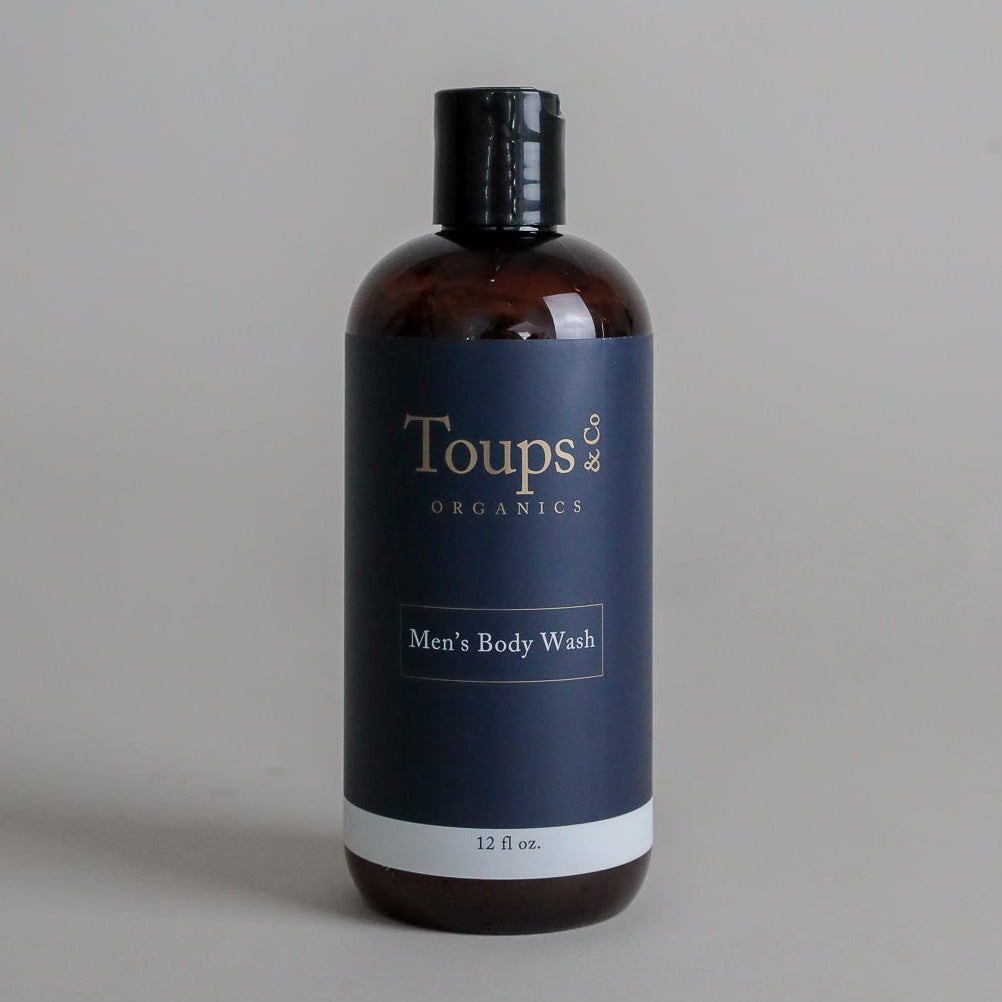 A brown plastic bottle labeled Toups and Co Organics Men’s Body Wash, 12 fl oz, with a black cap, is set against a plain light gray background, showcasing this sulfate-free body wash formulated for men.