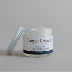 A glass jar of Toups and Co Organics Tallow Balm – Original, perfect for all-over hydration and calming dry, sensitive skin, sits on a simple light background with its lid removed.