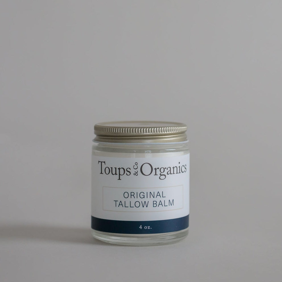 A glass jar of Toups and Co Organics Tallow Balm – Original with a metal lid, expertly formulated for nourishing whole-body moisture and ideal for dry, sensitive skin, displayed on a simple light grey background.