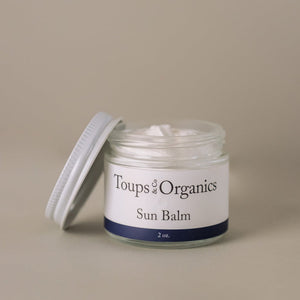 A glass jar of Toups and Co Organics Sun Balm with an open white lid, filled with white balm, rests on a neutral background, highlighting this natural sun balm formulated with non-nano zinc oxide.