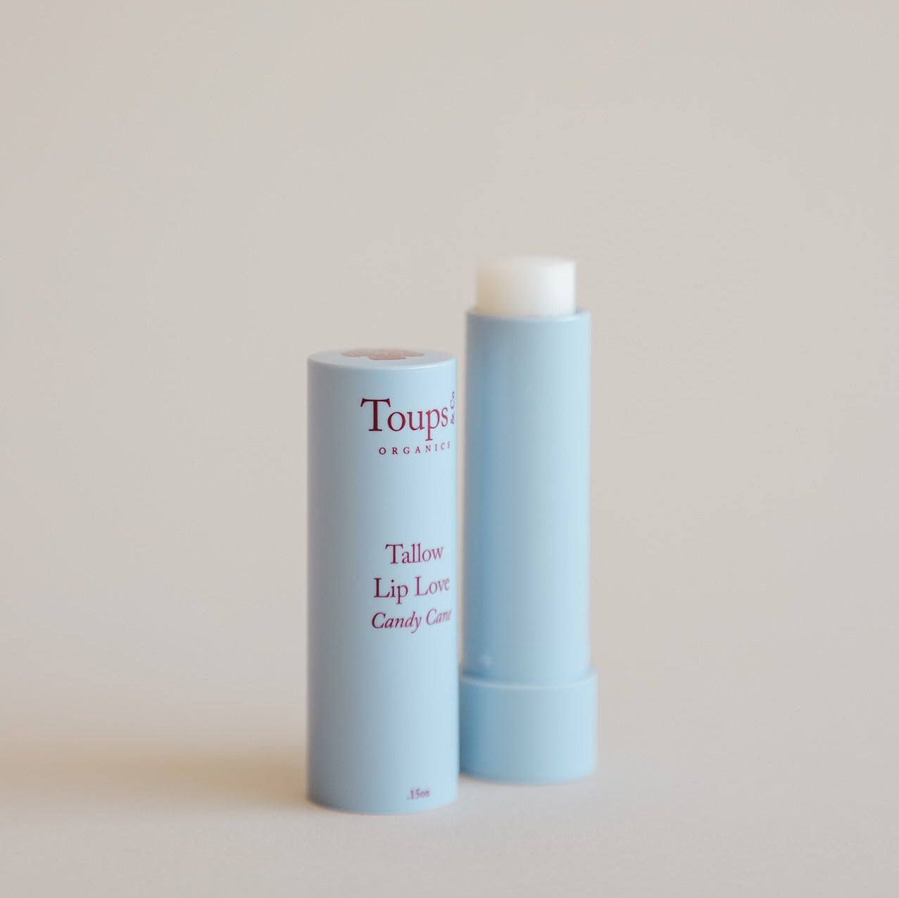 A blue tube of Toups and Co Organics Candy Cane Lip Love is displayed with its cap off and placed next to it.
