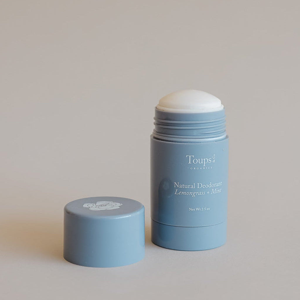 A blue tube of Toups and Co Organics Natural Deodorant is shown with its cap removed and placed beside it on a neutral background.