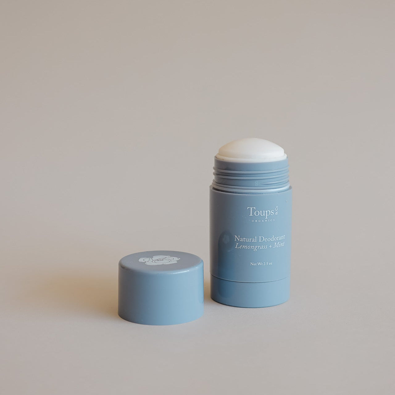 A blue tube of Toups and Co Organics Natural Deodorant is shown with its cap removed and placed beside it on a neutral background.