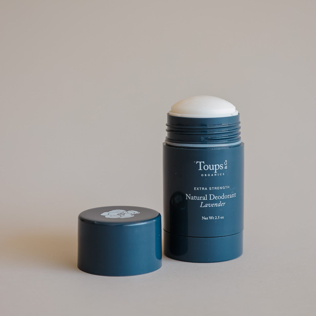 A blue tube of Toups and Co Organics Natural Extra-Strength Deodorant, cap off and placed beside it, is displayed on a neutral background.