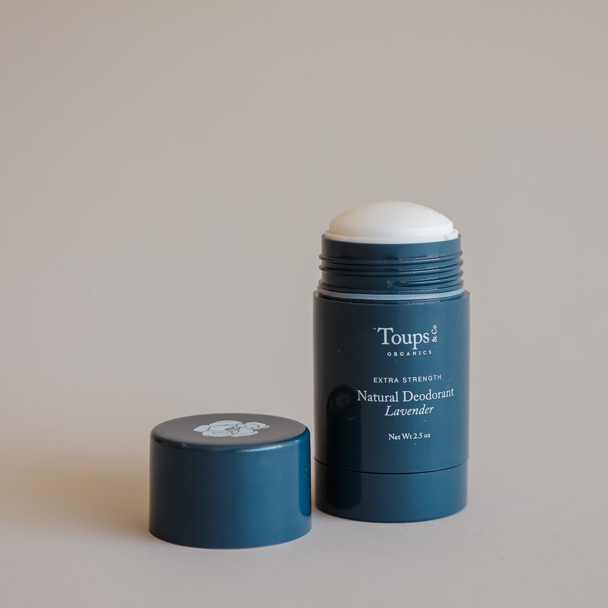 An open blue tube of Toups and Co Organics Natural Extra-Strength Deodorant for sensitive skin in lavender scent sits on a neutral background with the cap beside it.