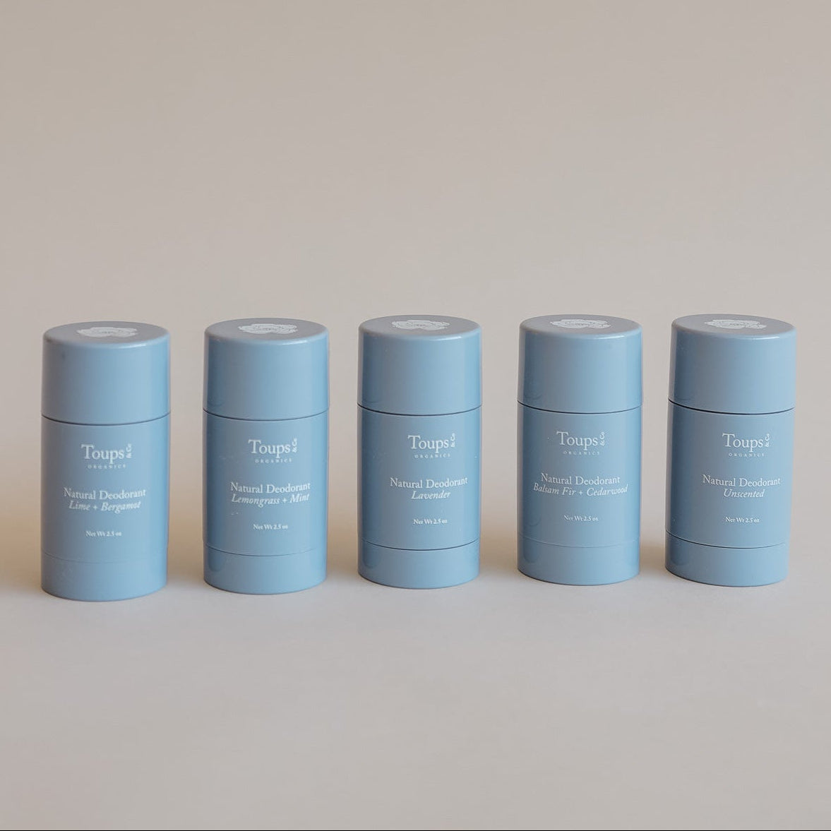 Five light blue cylindrical containers from Toups and Co Organics’ Non Toxic Starter Set stand in a row, each displaying a different scent on the front.