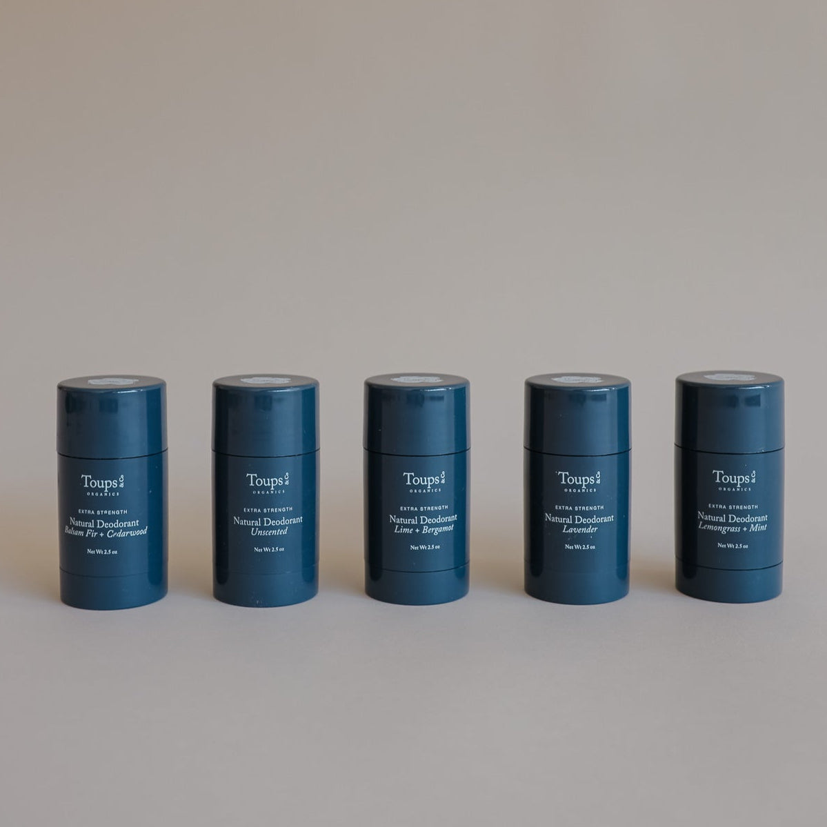 Five blue cylindrical containers of Toups and Co Organics Natural Extra-Strength Deodorant, specially formulated for sensitive skin, are arranged in a row against a plain neutral background.