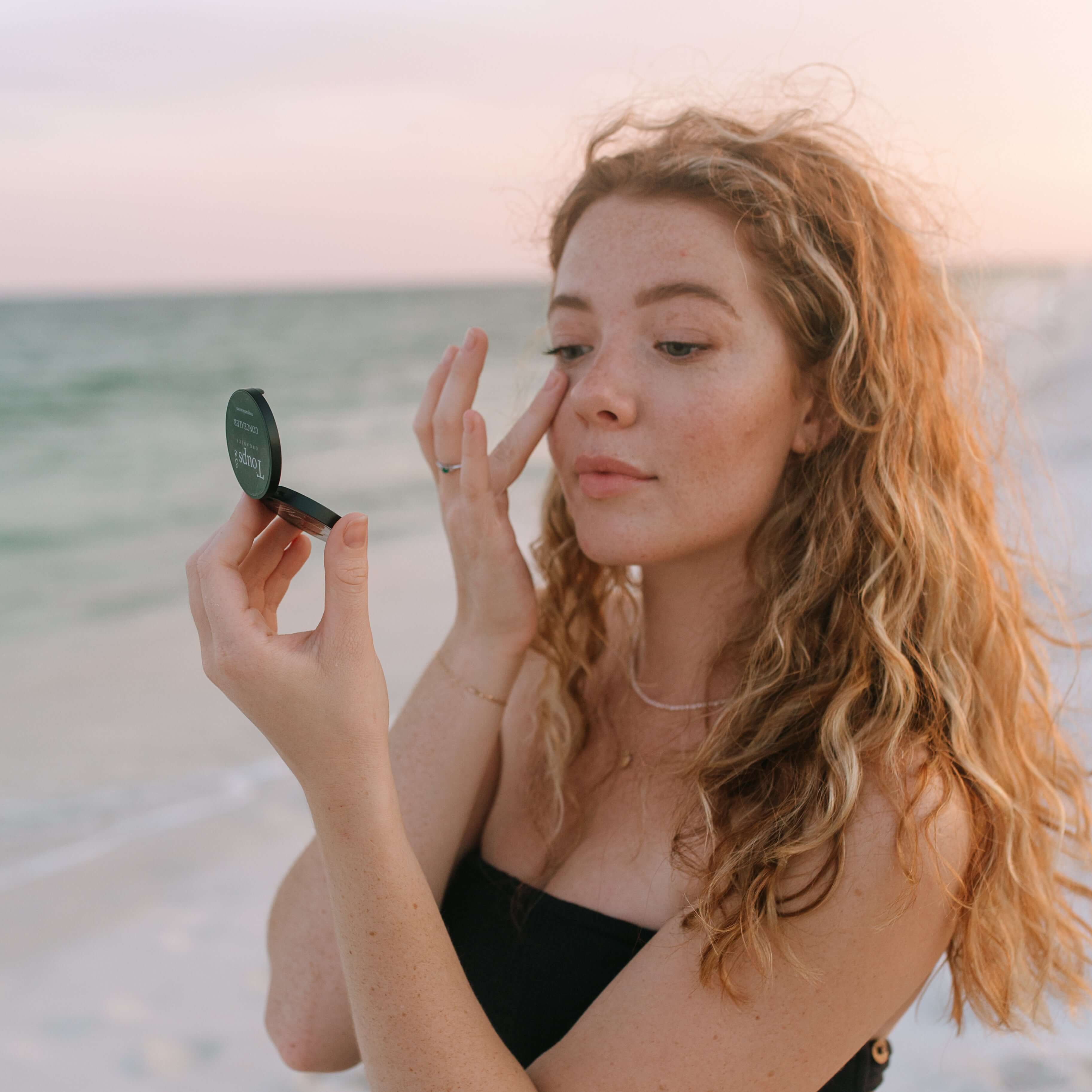 young-woman-applies-cream-concealer-to-under-eyes-with-ocean-background