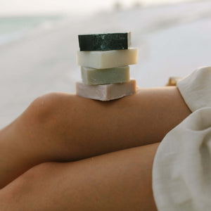 woman-holds-tallow-soap-and-coconut-oil-soap-against-beach-background
